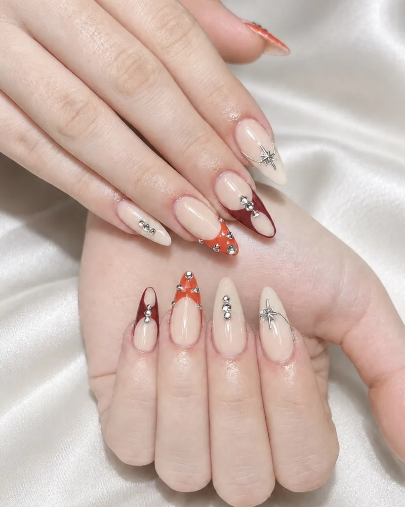 Nude almond nails with red and orange French tips and silver studs at Chillux Nails, Orpington